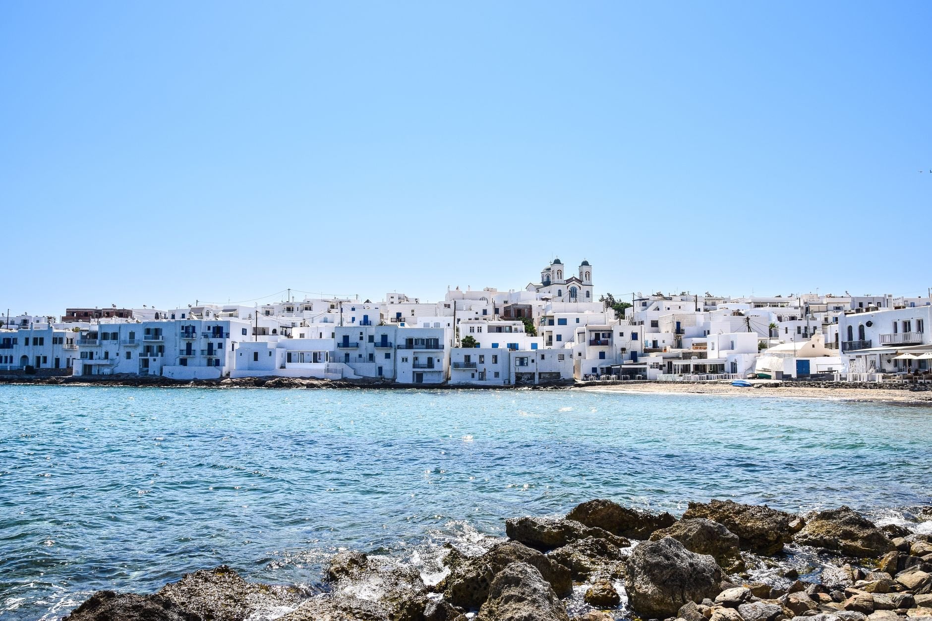 Whitewashed buildings and a church by the sea in a Greek town under a clear blue sky